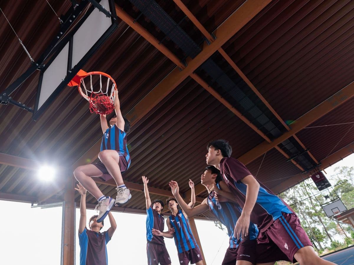 屋根付きコートでダンクシュートを決めるJohn Paul Collegeのバスケットボール部員